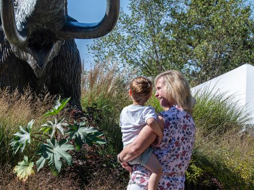 An employee and her child admire the bronze mastodon statue on the Alumni Plaza.