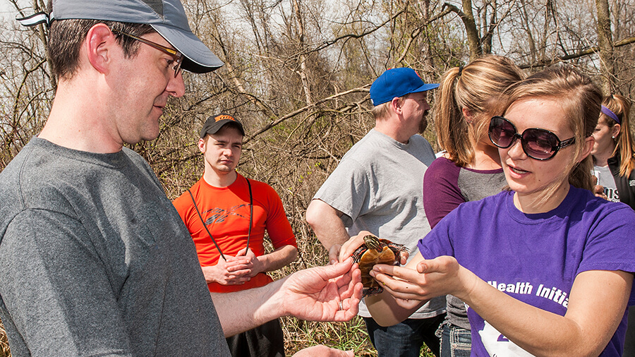 A student holds up a turtle while their professor analyzes it.