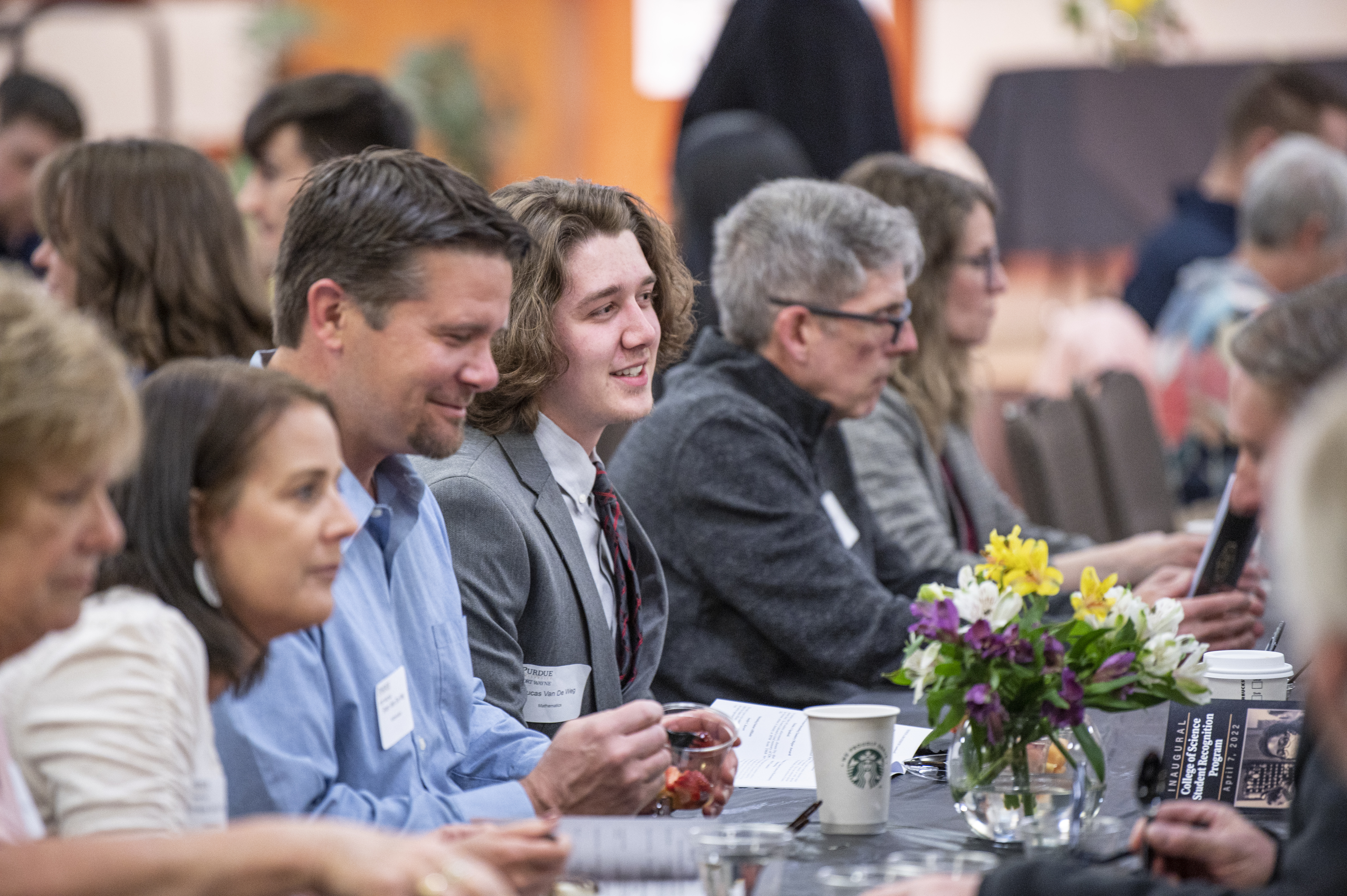 One male student in the foreground, six total, sitting at a table for a recognition event