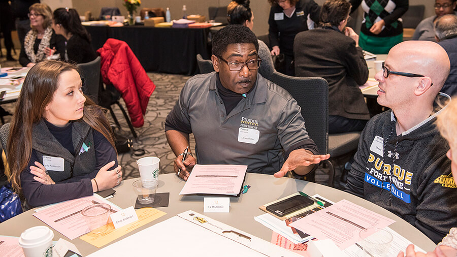 Three strategic planning session attendees talk to one another at a round table.