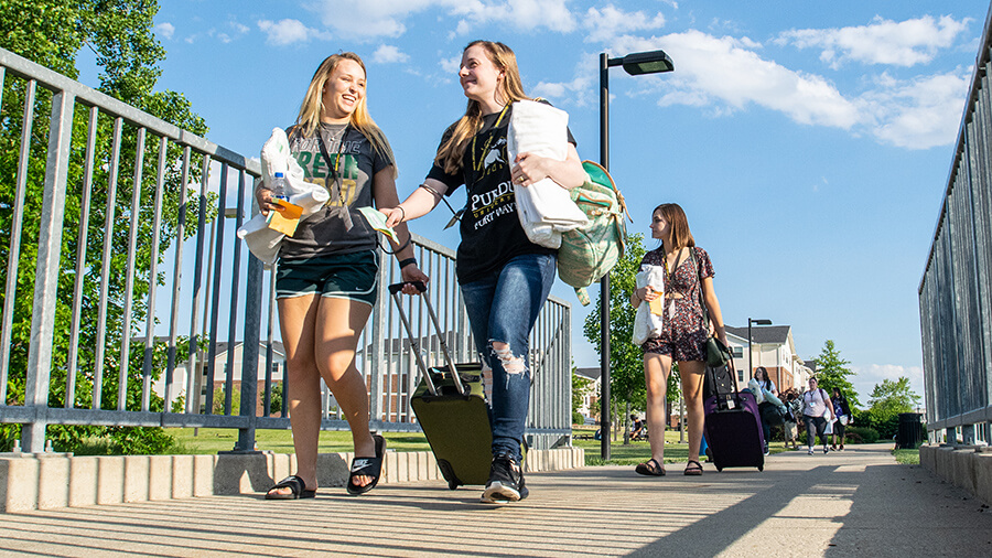 Students walking on the Waterfield Campus with a suitcase.