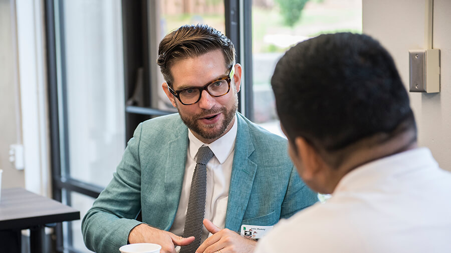 Two new faculty members talk to one another at a table.