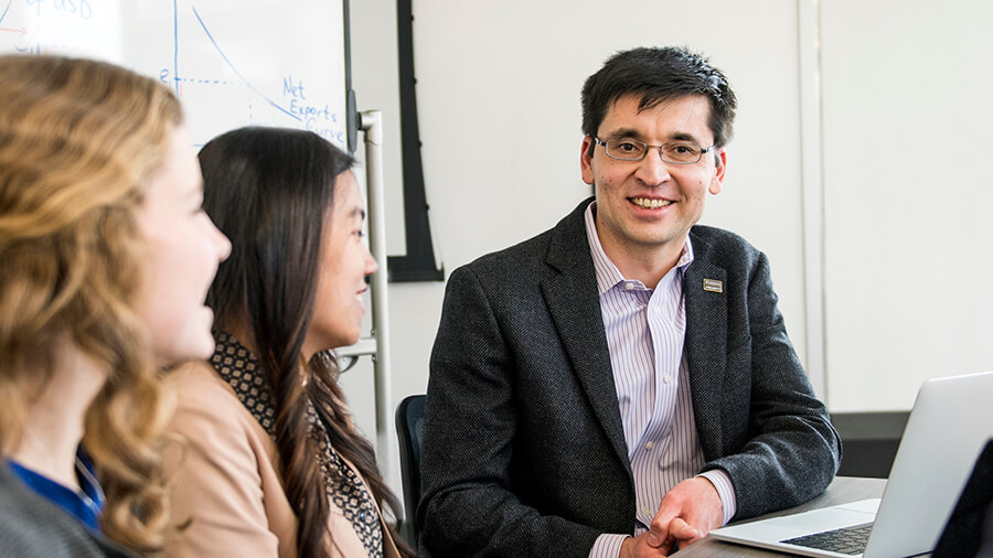 One faculty member smiles while sitting at a laptop among two other faculty members.