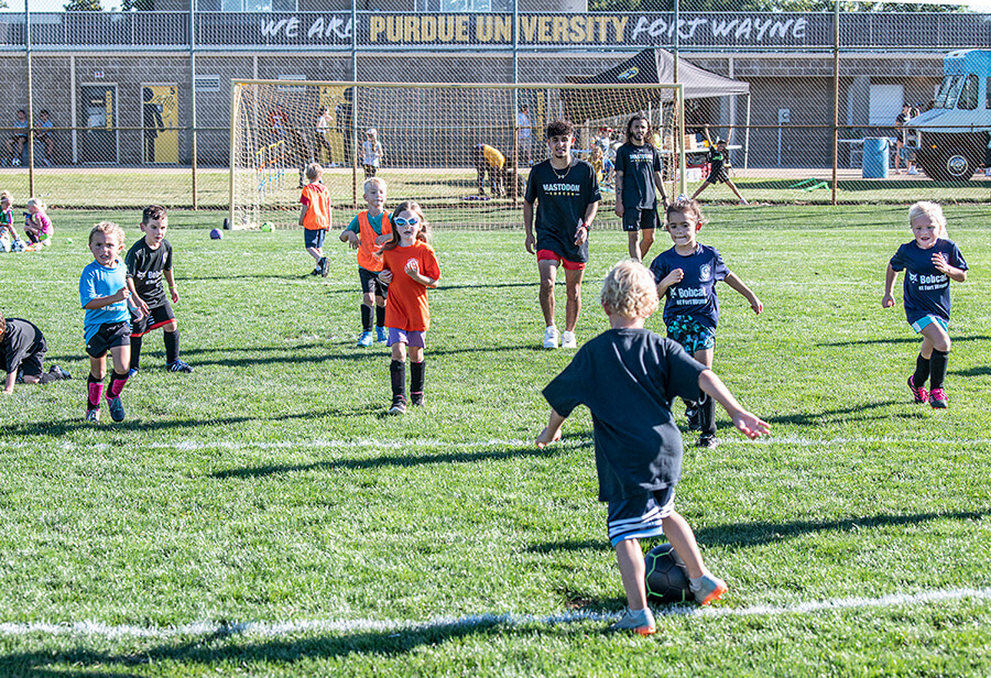 A group of young kids play soccer with college students.