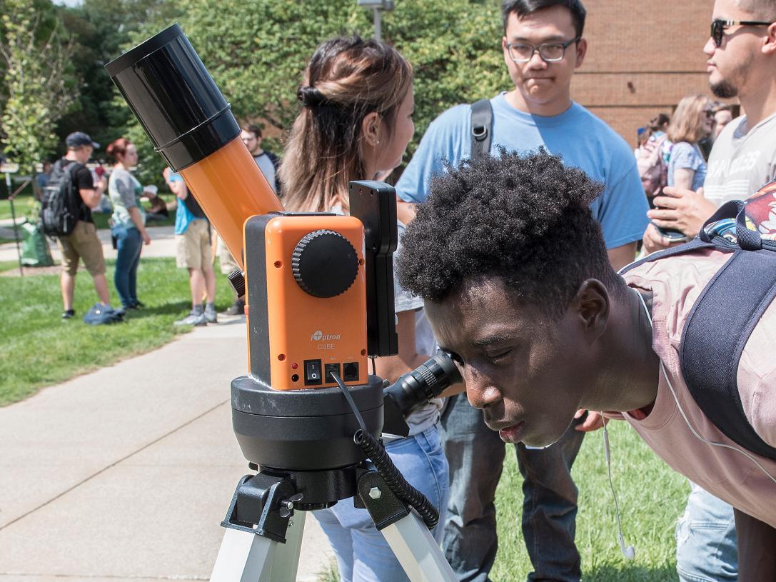 Student looks into a telescope at an eclipse party on campus.