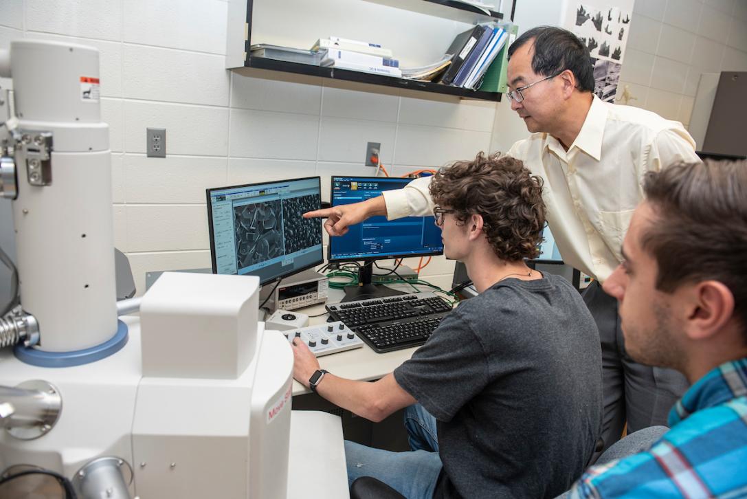 Professor and students working on a computer in an engineering lab.