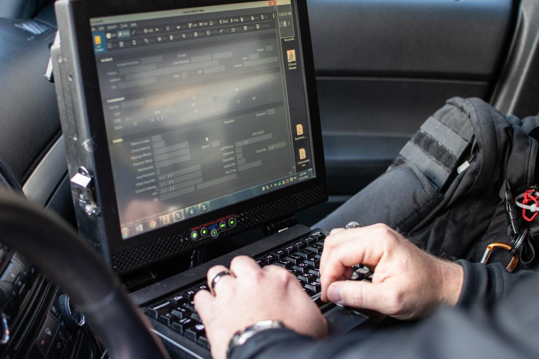 Police office typing on a laptop in a cop car.