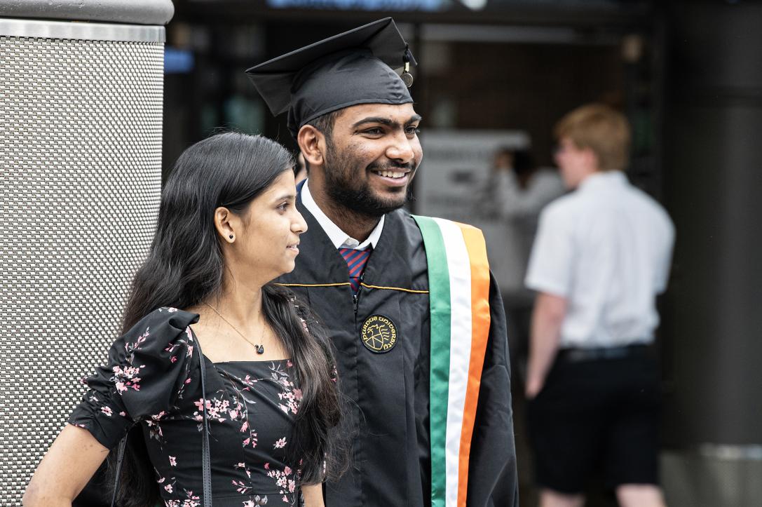 Graduating student smiles and poses with commencement guest.