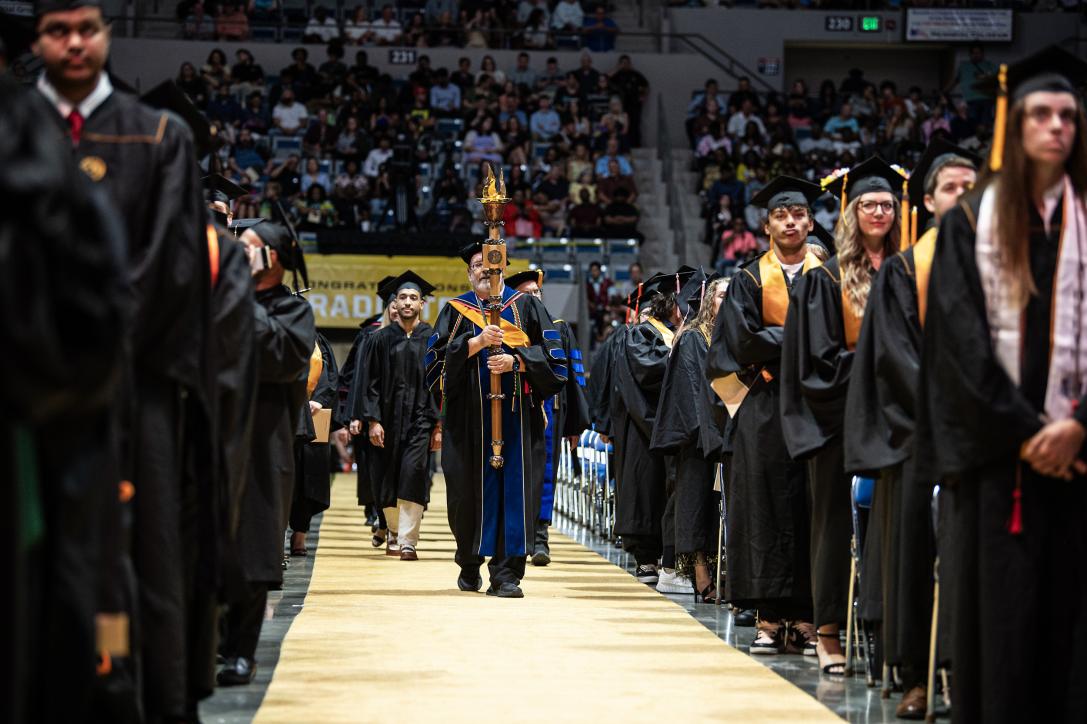 Students stand at their seats in the arena at commencement.