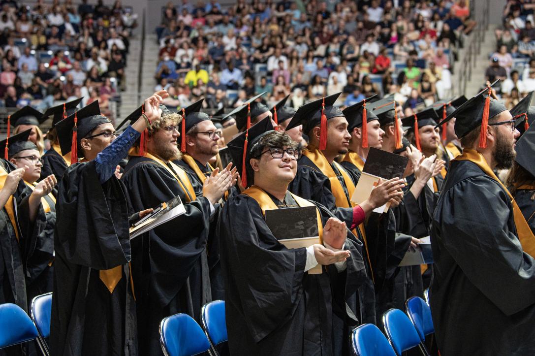 Students stand and clap at commencement.