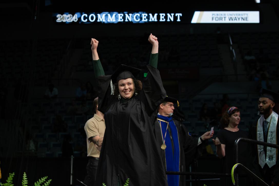 Excited graduating student raises arms in the air.