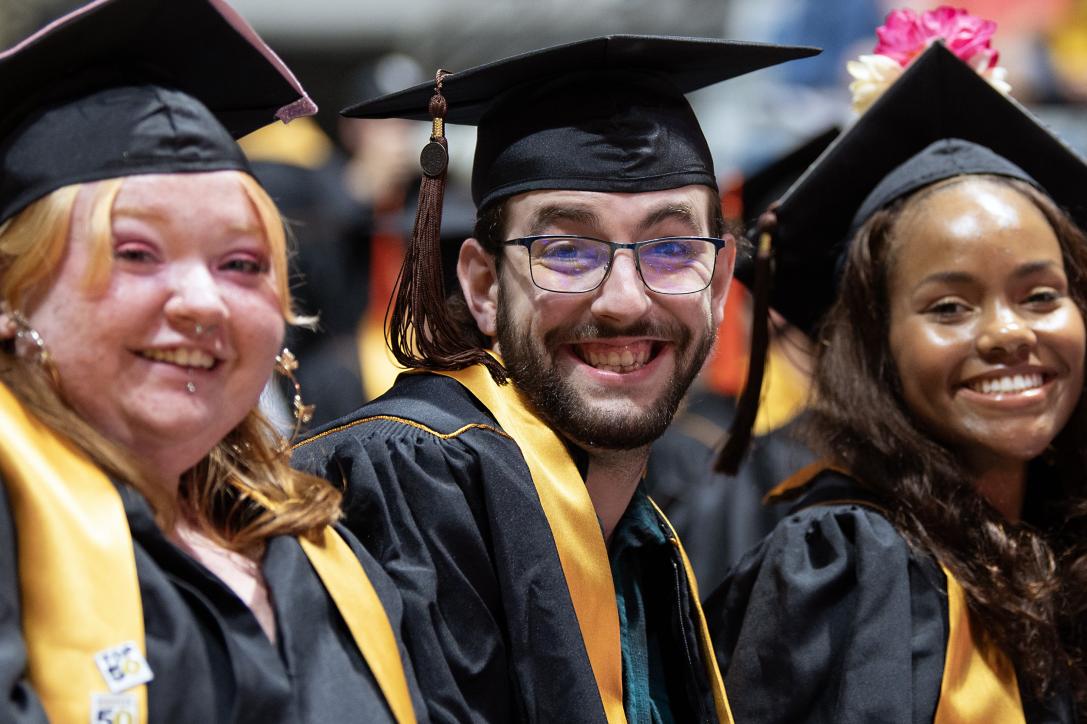 Three students in caps and gowns smile for the camera.