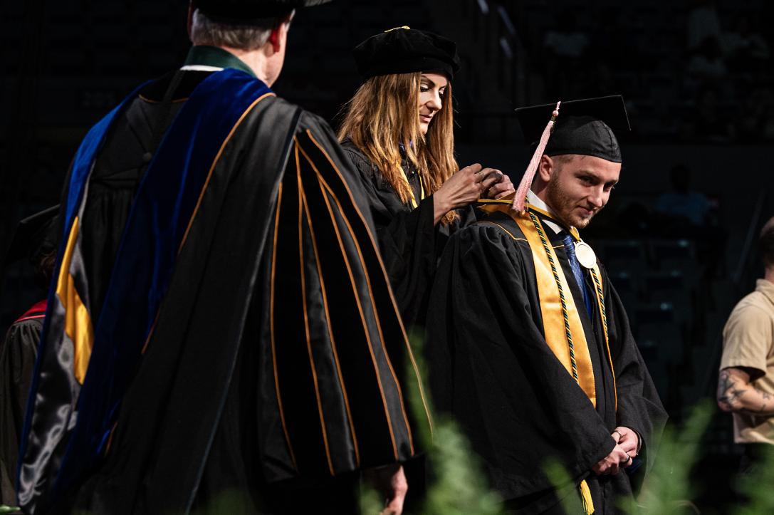 Graduating student on stage with faculty.