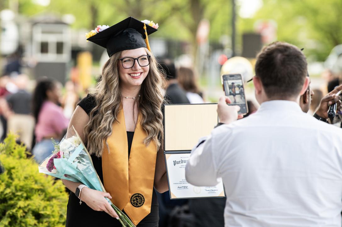 Graduated student poses with flowers and degree holder.