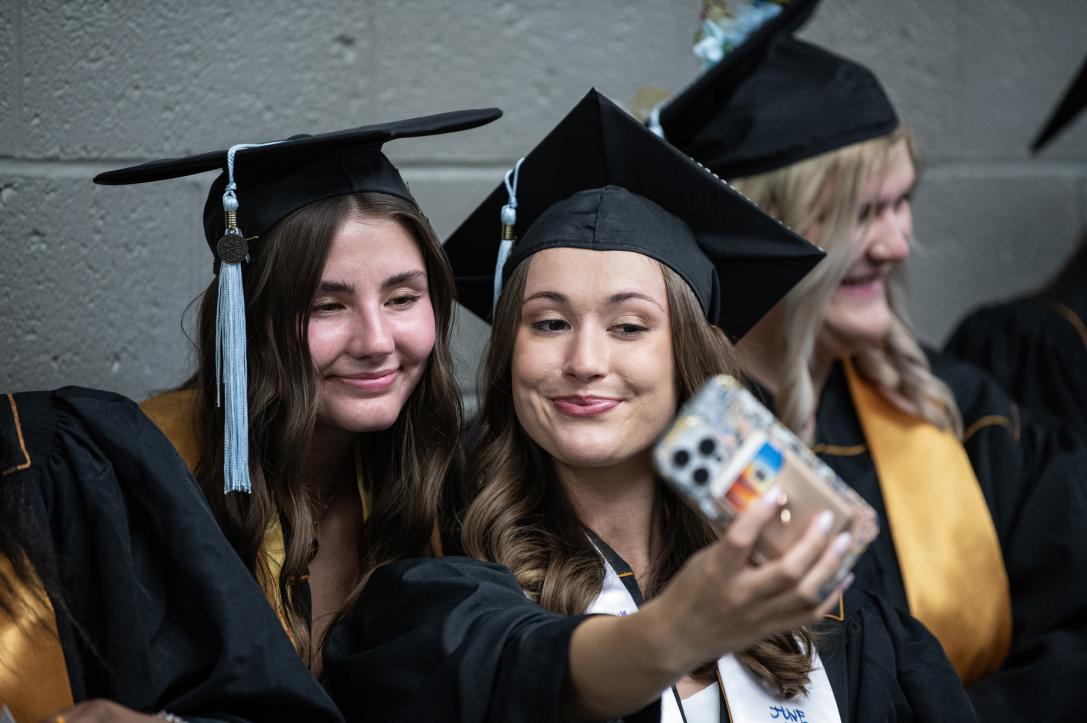 Students in caps and gowns take a selfie.