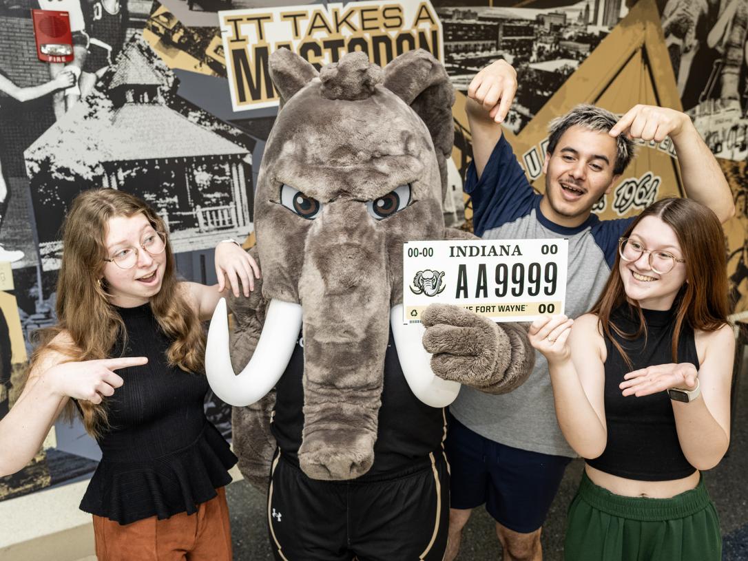 Three students pose with Don to show off a PFW license plate