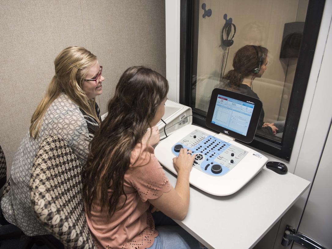 Communication science and disorders students testing a subject's hearing in a mock lab setting.