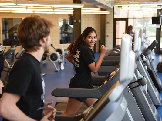 A pair of students are running on treadmills in the Gates Center fitness studio.