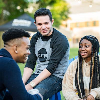 Three students chat amicably while sitting in Adirondack chairs