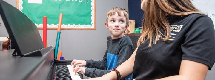 A music therapy student plays piano with a young student.