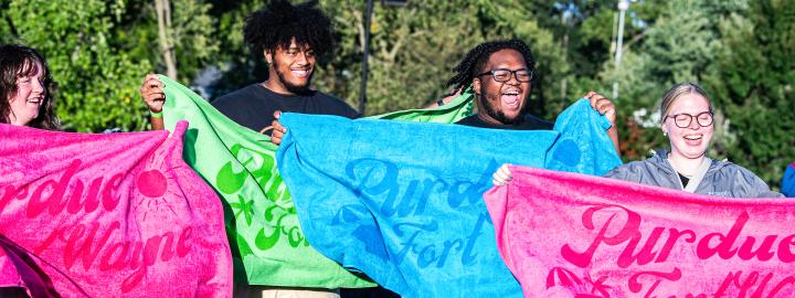 Students holding up PFW beach towels at the Student Housing foam party.