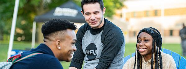 Three students chat amicably while sitting in Adirondack chairs