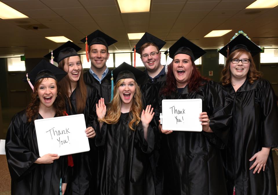 Students in cap and gowns hold signs with "Thank You!" written on them.