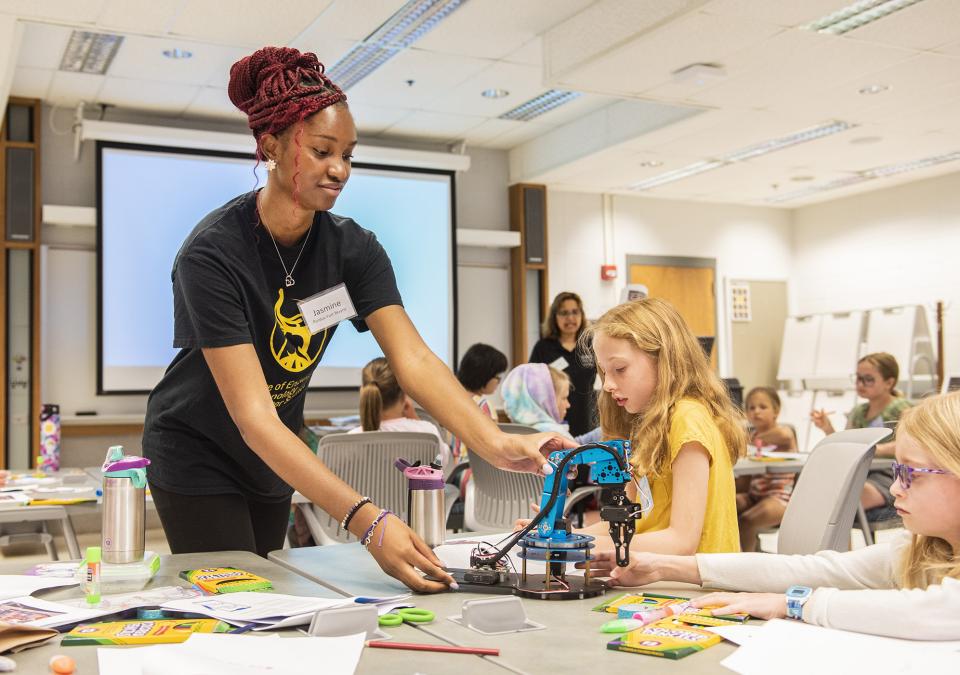 A student and teacher work with a robotic arm