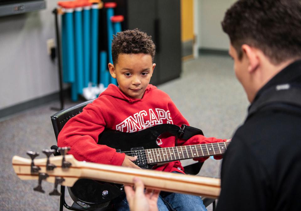 A music therapy student is playing guitar with a young boy.