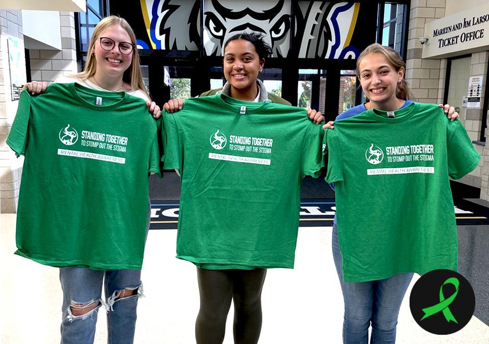 Female students holding green Mental Health Awareness Week T-shirts