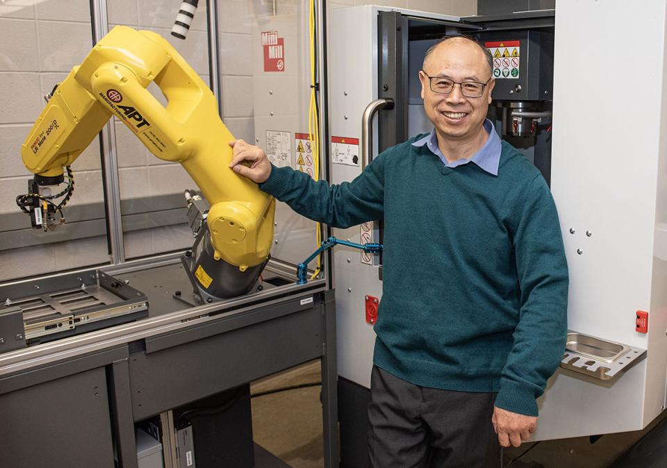 Zhuming Bi is standing next to a robotic arm