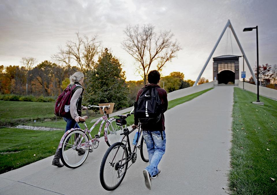 A male and female student walking their bikes to the university