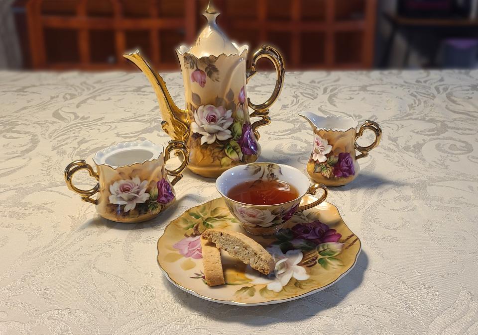 Antique tea set with pink and white roses on a brown-beige background serving tea and two small biscotti 