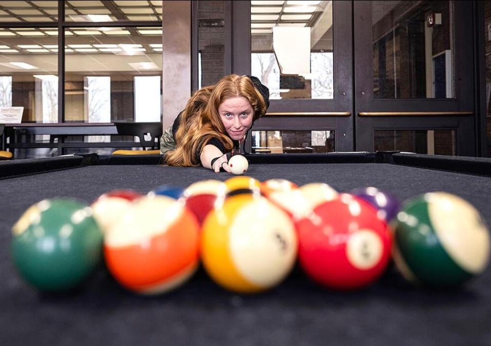 A female student is breaking a rack on a pool table.