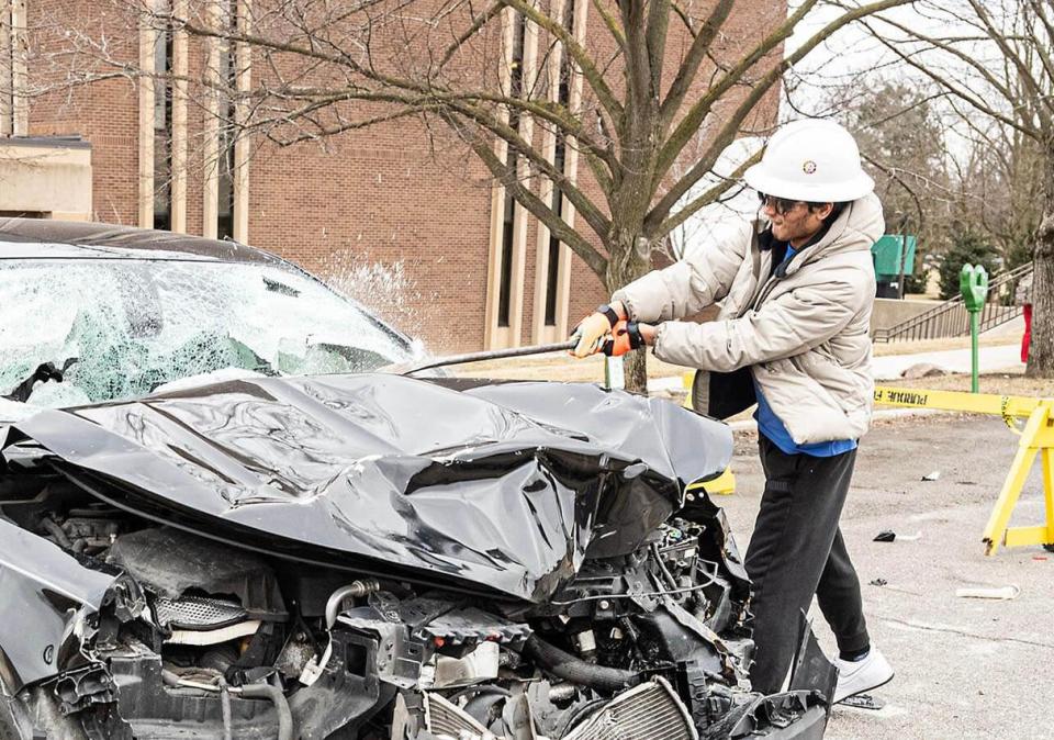 A student in a hard hat is smashing a car with a sledgehammer