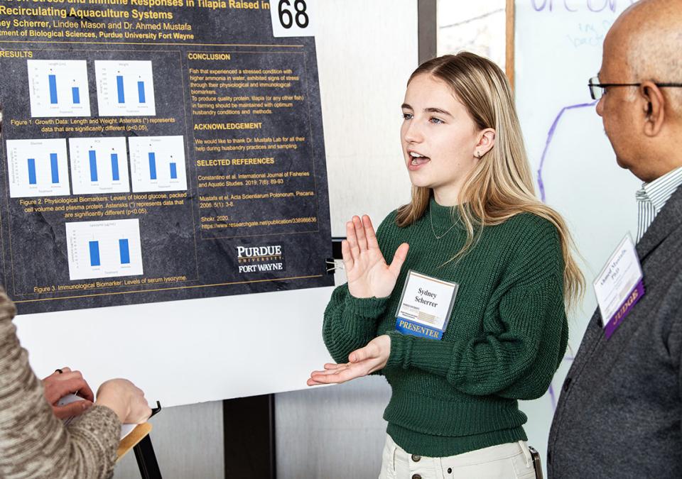 A student explains her research project to a judge at the symposium