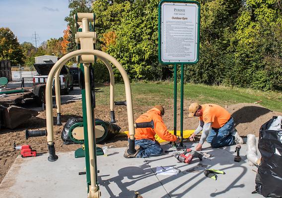 Facilities Management workers finish installation of ouutdoor fitness station on main campus.jpeg