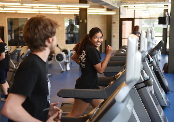 A pair of students are running on treadmills in the Gates Center fitness studio.