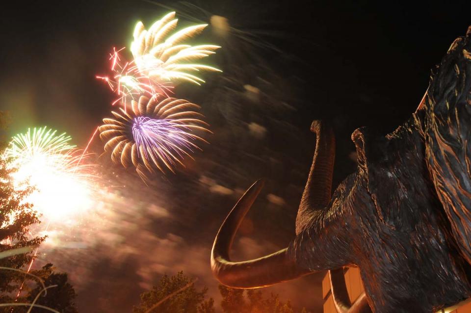 Fireworks light up the night sky in front of the bronze mastodon statue