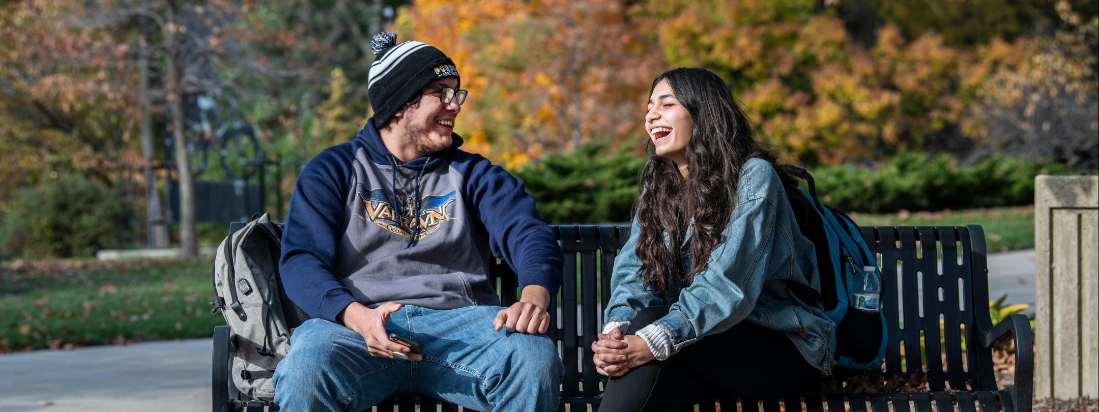 Students laughing during a conversation on a bench on campus.