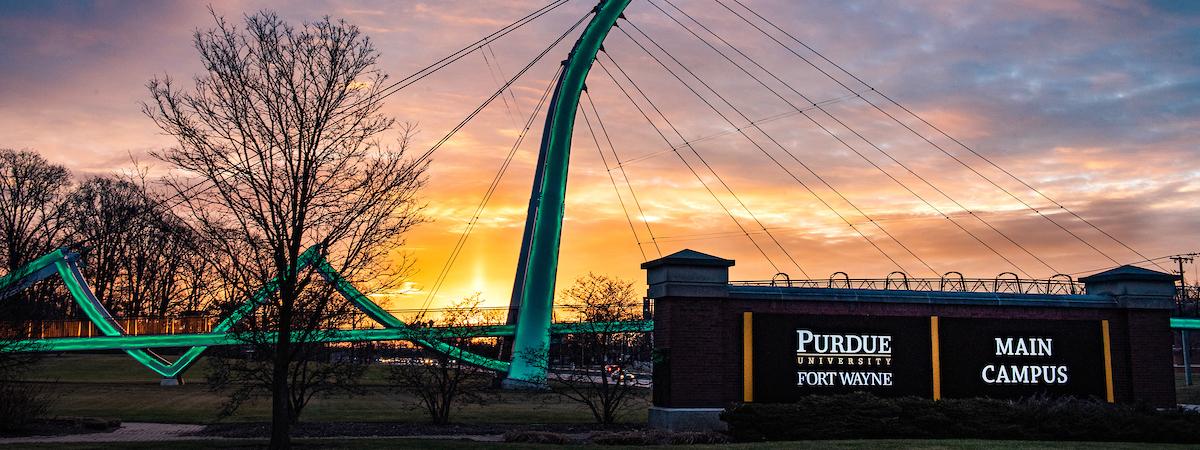 Campus sign with the bridge and a sunrise in the background.