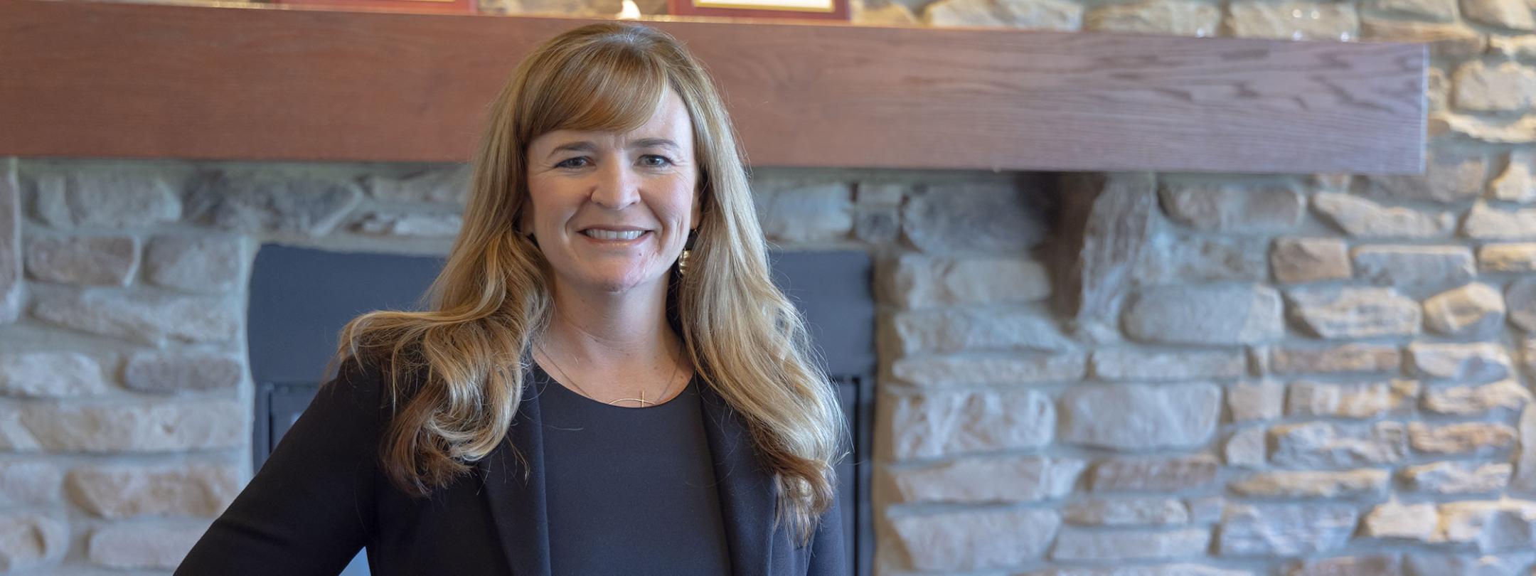 Portrait of Kim Grannan standing in front of a fireplace in the Alumni Center.