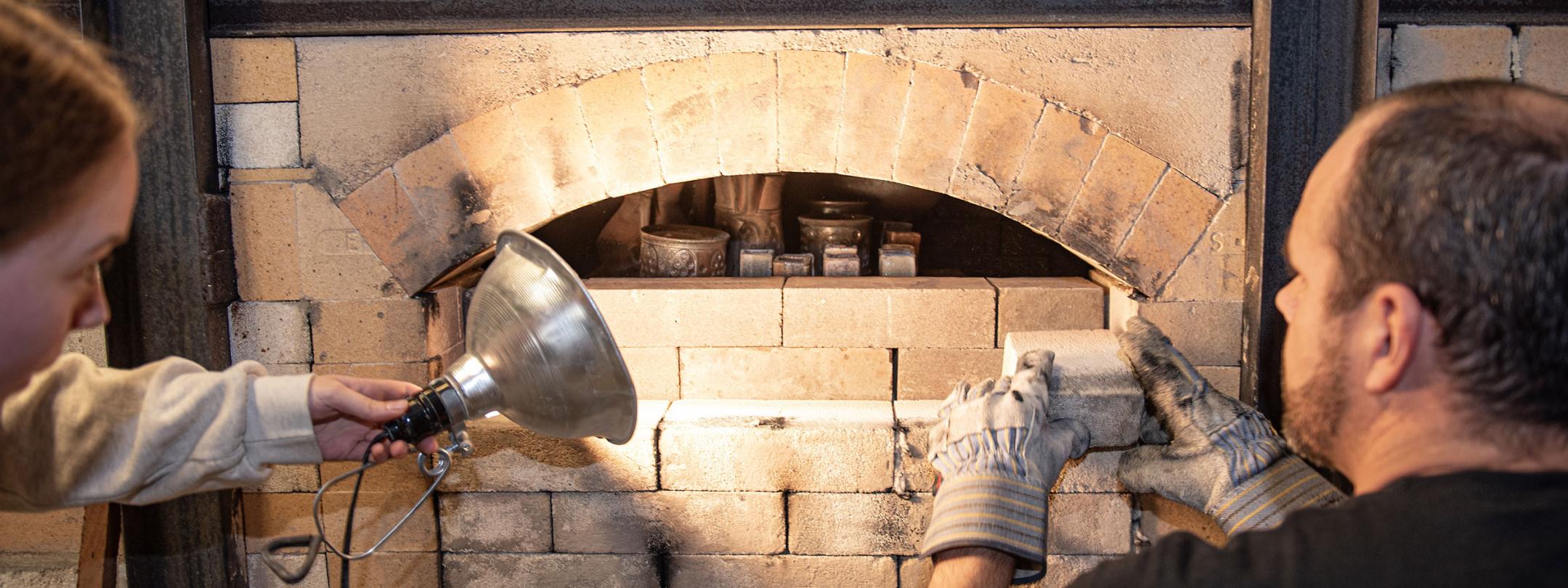 Two people are loading a wood burning kiln