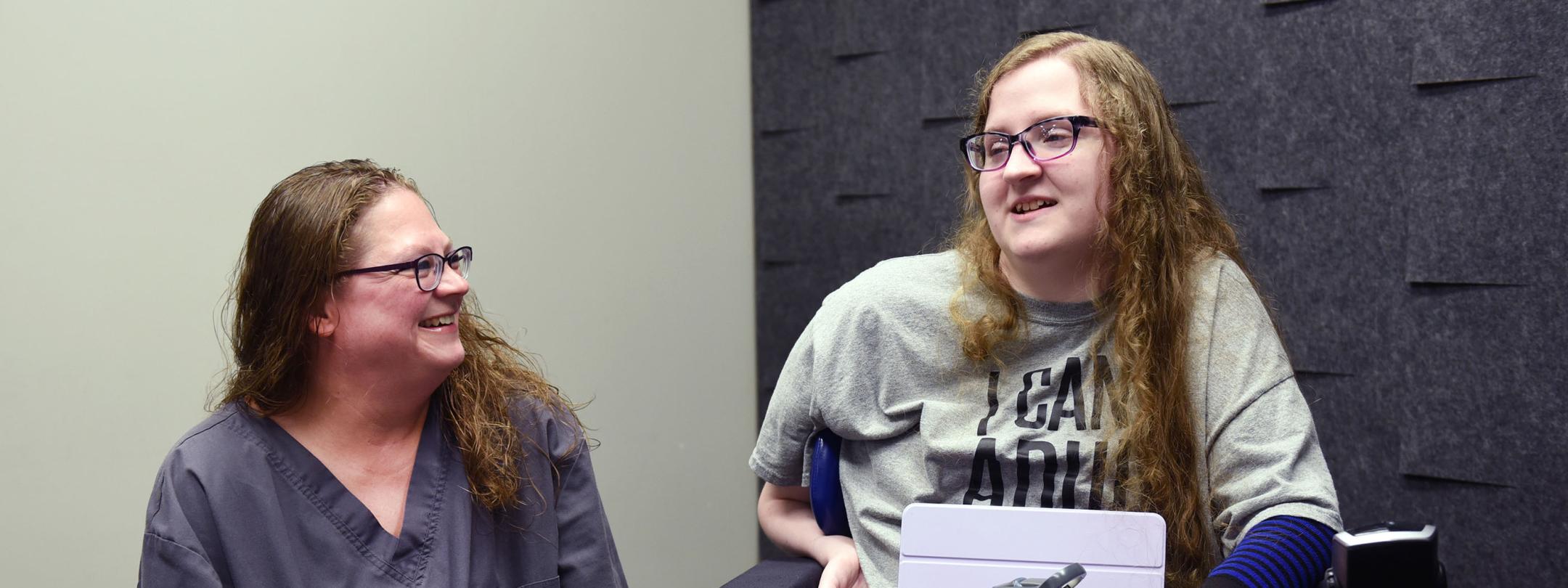 Elizabeth Farlow is seated in a wheelchair and speaking to a friend.