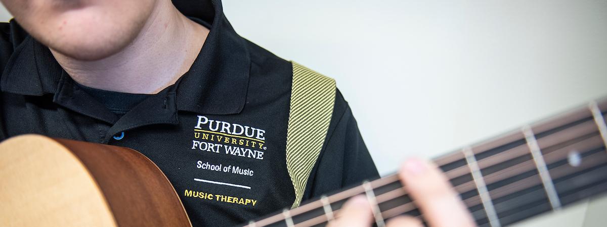 A student in a School of Music polo plays an acoustic guitar.