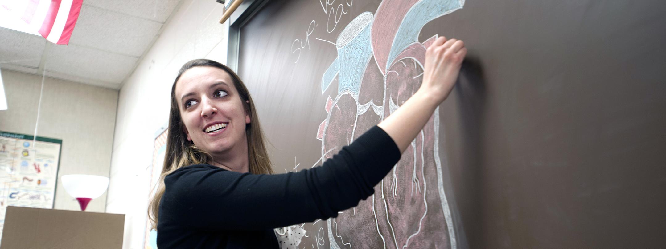 A female teacher writes on a chalkboard