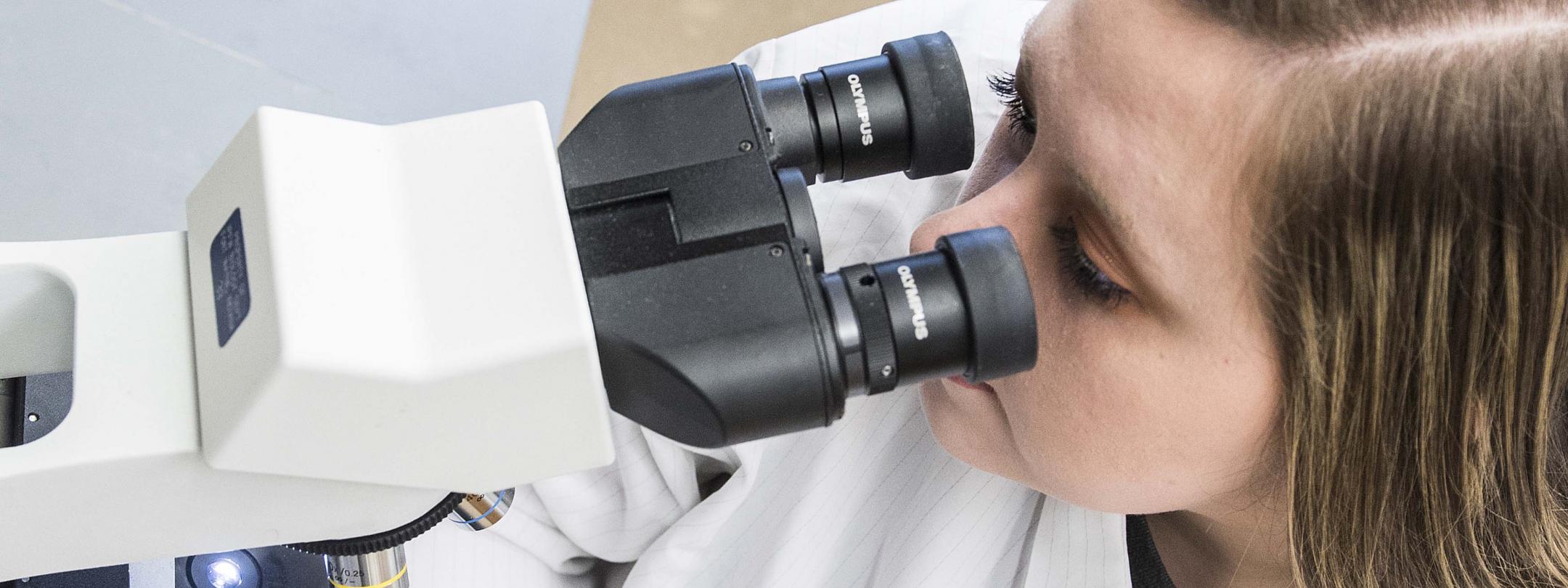 Biology student examining a slide sample on a lab microscope.