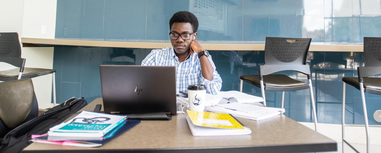 Graduate student studying with a laptop and books.