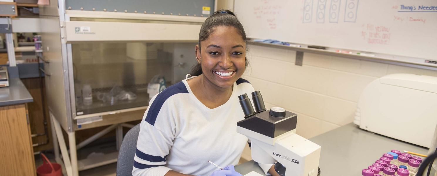 Biology student examining a slide sample on a lab microscope.