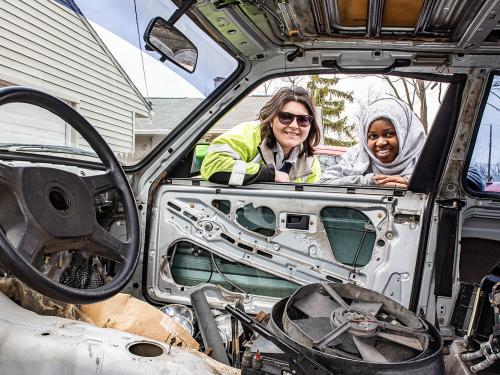 Two polytechnic students looking through the window of the BMW car they're working on.